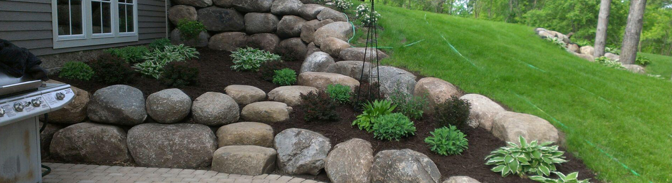Fieldstone Boulder Retaining Wall and flower planter running along the side and back of a residential home