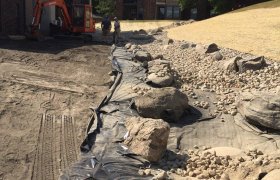 Excavating crew working on a rock drainage area between two apartment complexes