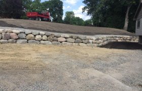 Short but long boulder retaining wall running along the driveway of a new house