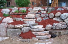 Newly finished boulder retaining wall and plant garden complete with red mulch and cut boulder stairs