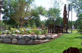 Raised flower garden with boulder retaining wall next to a backyard patio