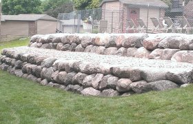 Tiered fieldstone retaining wall and landscape on the backside of an outdoor public pool