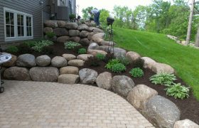 Boulder retaining wall used to hold back the ground around a sunken paver patio