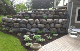 Multi-tiered flower garden and boulder retaining wall along the side of a residential home
