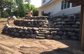 Multi-level boulder retaining wall with cut boulder steps connecting each tier