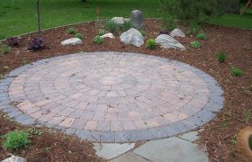 Circular paver patio area surrounded by mulch and flowering plants